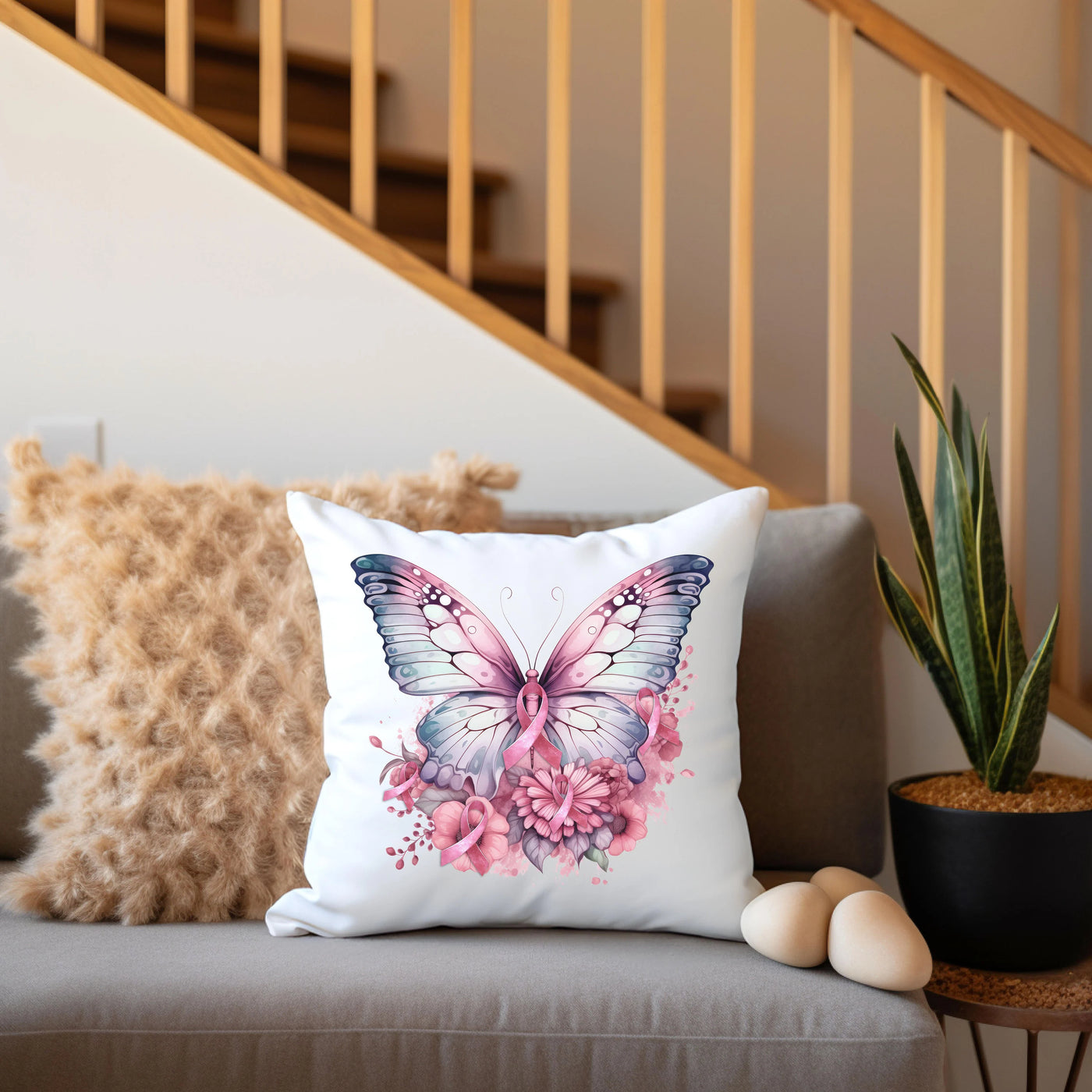 White cushion with a colorful butterfly design placed on a sofa next to a plant and decorative pillows, with wooden stairs in the background.