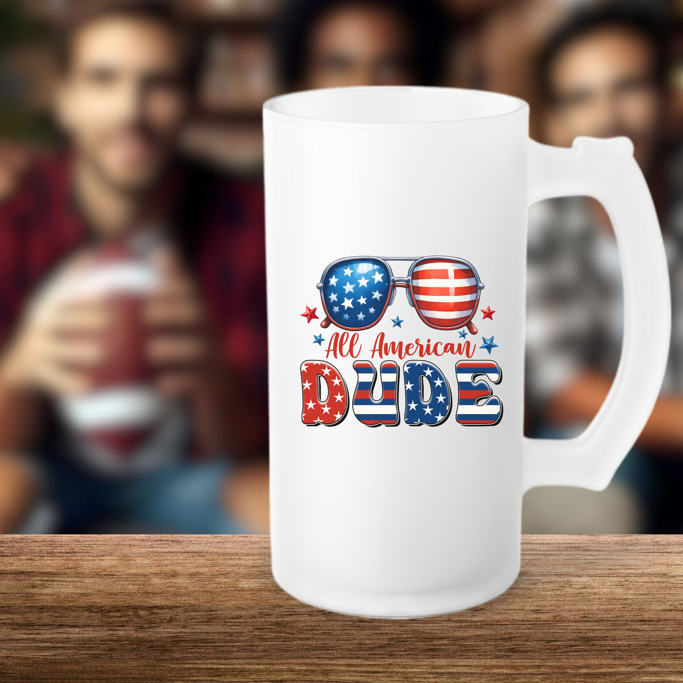 Frosted beer mug with "All American Dude" design featuring sunglasses with American flag, on a wooden table with blurred friends in the background