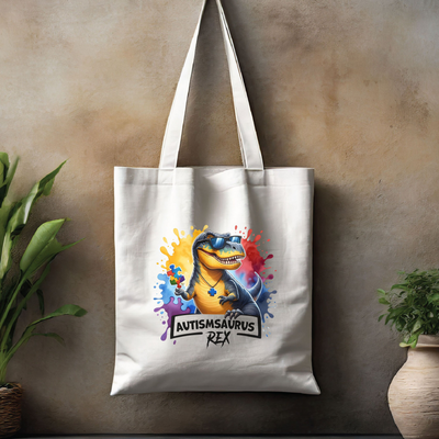 White tote bag with colorful Autismsaurus Rex dinosaur graphic, displayed against a textured wall with plants on either side.