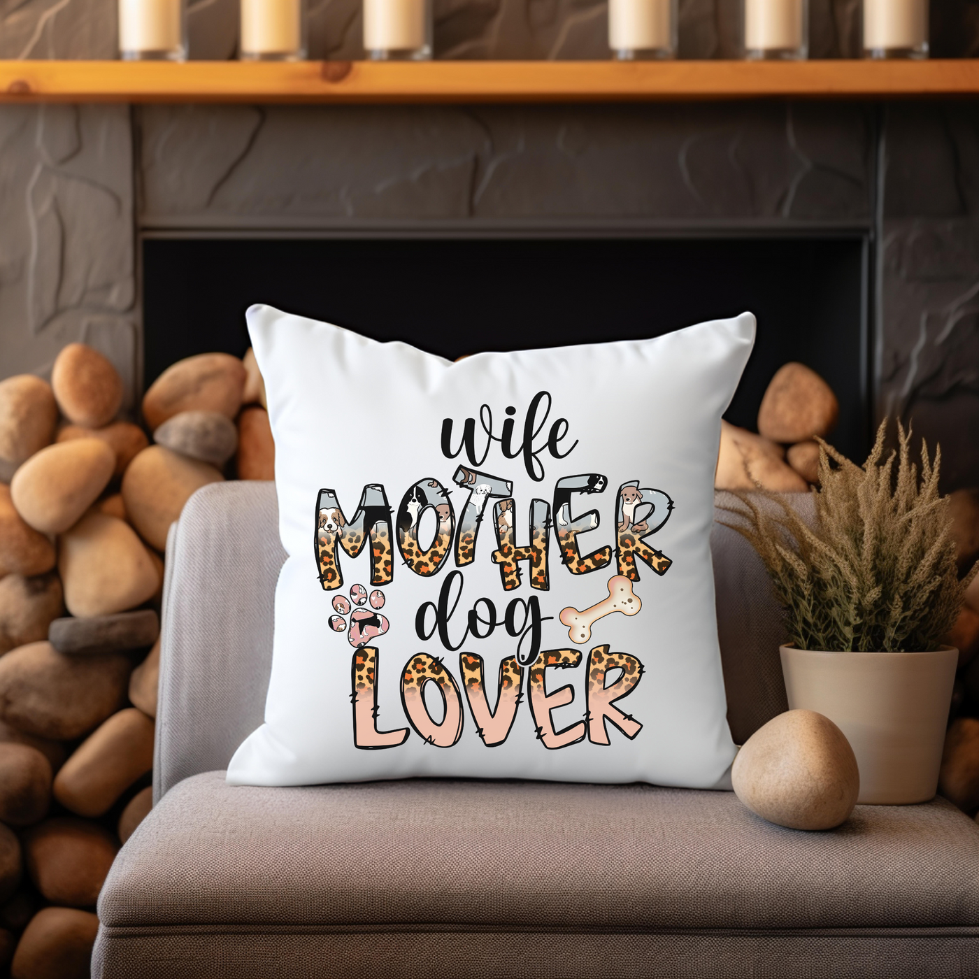 White pillow with text "Wife Mother Dog Lover" on a cozy chair by a fireplace with candles and stones in the background