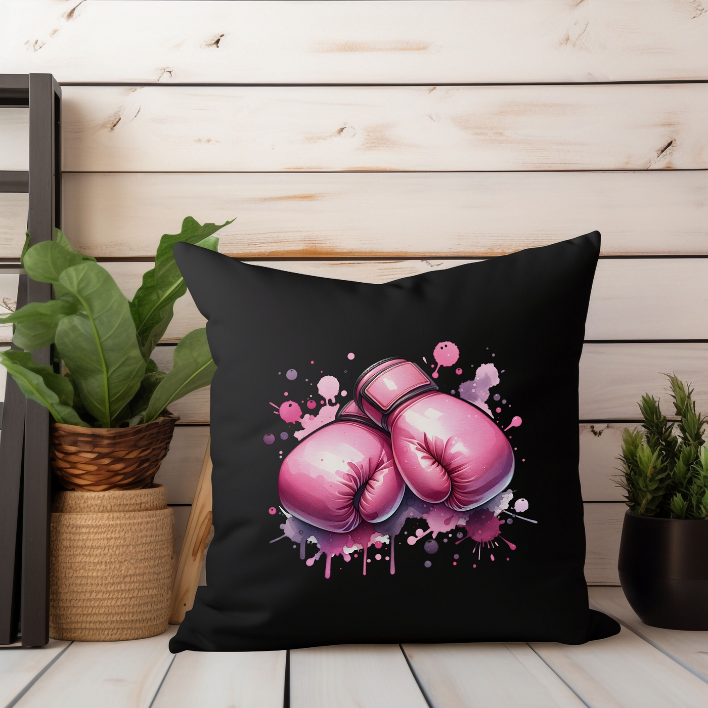 Stylish black pillow with pink boxing gloves design on a wooden shelf, decorated with potted plants.