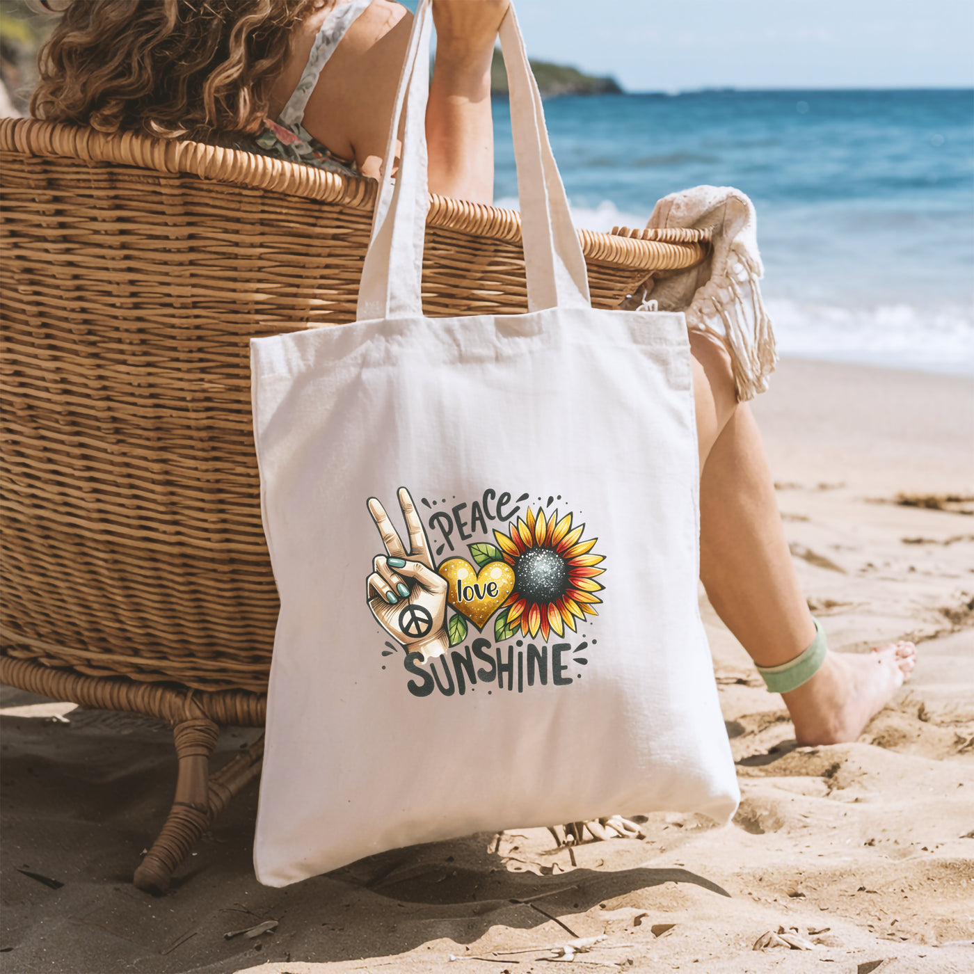 Woman sitting on wicker chair at beach with tote bag featuring peace, love, and sunshine design.