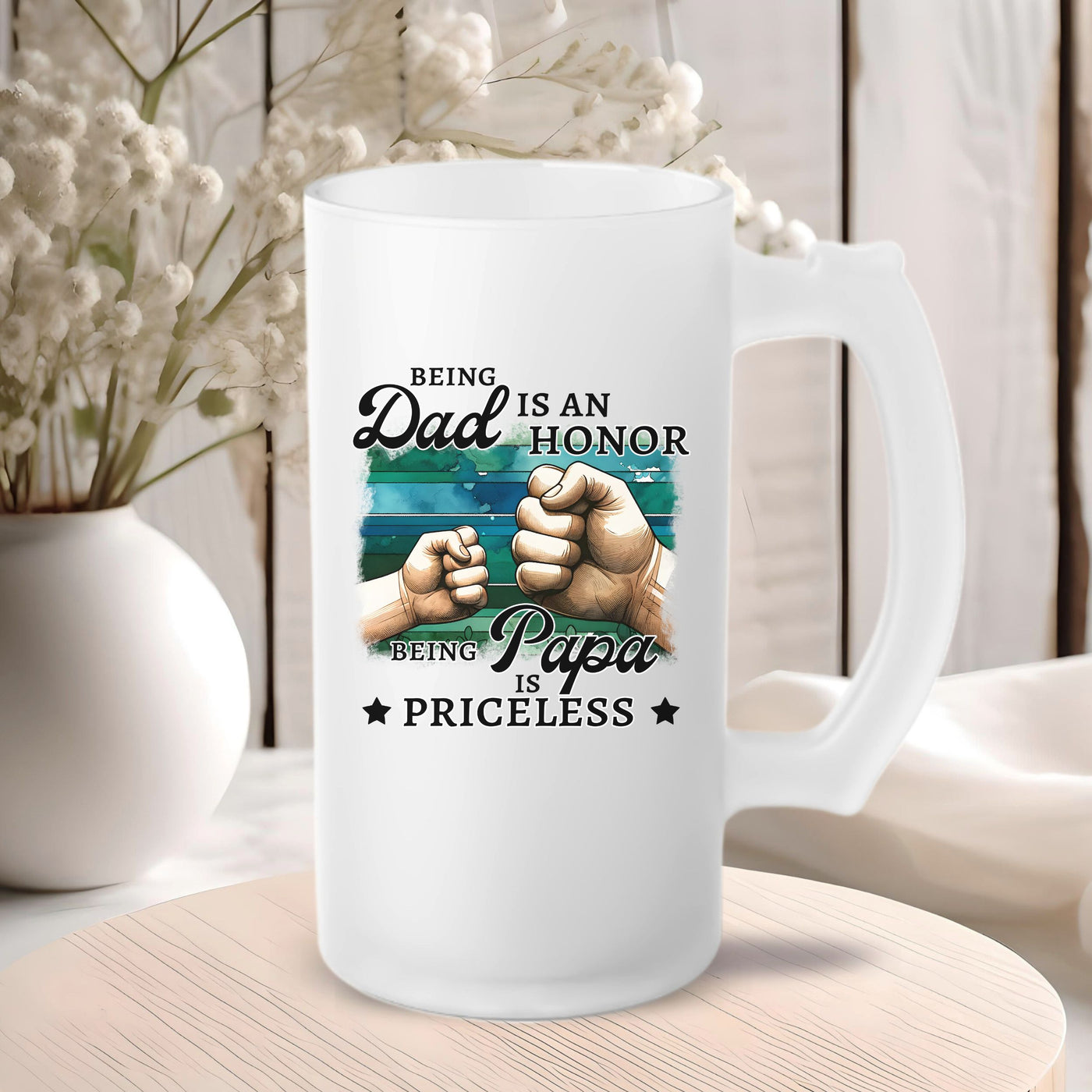 Frosted glass mug with "Being Dad is an Honor, Being Papa is Priceless" text and fist bump design, placed on a wooden table with flowers in the background