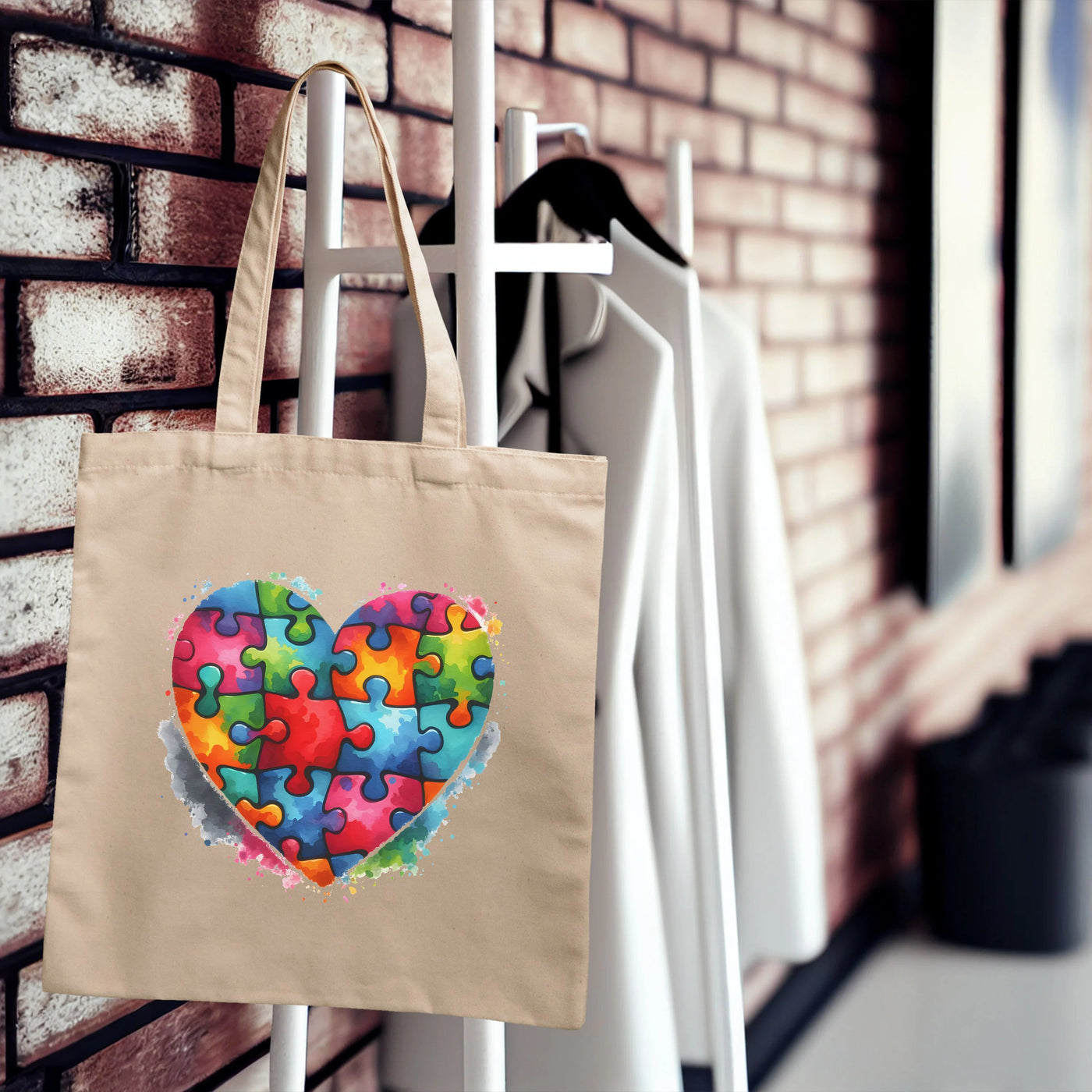 Beige tote bag with colorful heart-shaped puzzle piece design hanging on a coat rack with white coats in a stylish room.