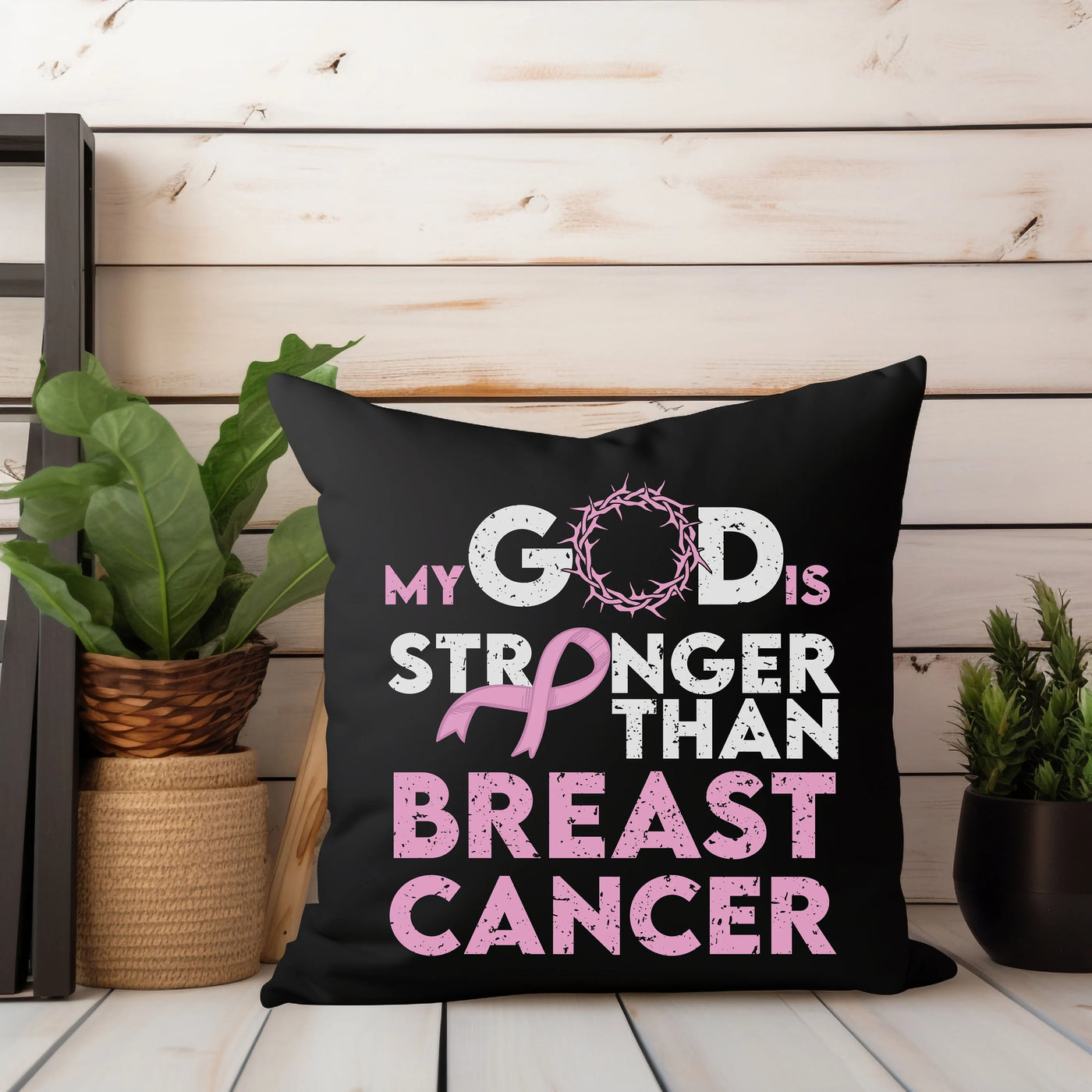 Inspirational pillow with "My God is Stronger than Breast Cancer" message in pink and white text, surrounded by plants and decorations.