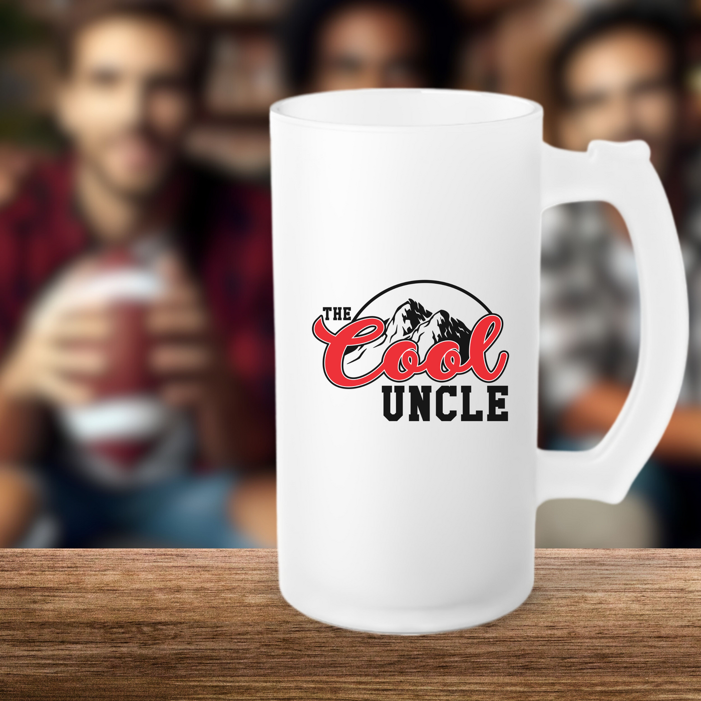 Frosted beer mug with "The Cool Uncle" logo placed on wooden table, blurry background of people holding football.