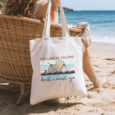 a woman sitting in a chair on the beach with a tote bag