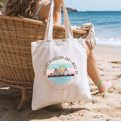 a woman sitting in a chair on the beach with a tote bag