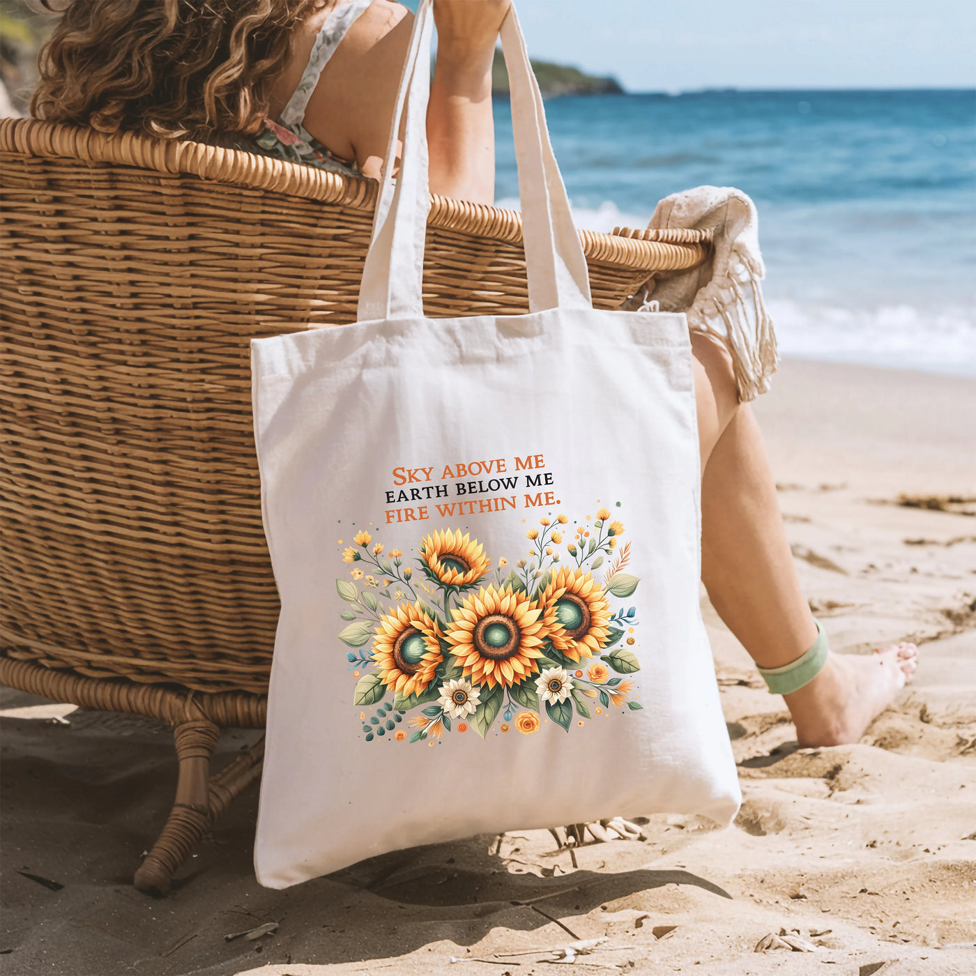 a woman sitting in a chair on the beach with a sunflower tote bag