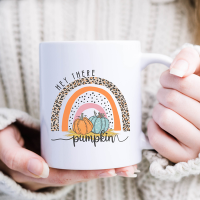 a woman holding a white coffee mug with a pumpkin on it