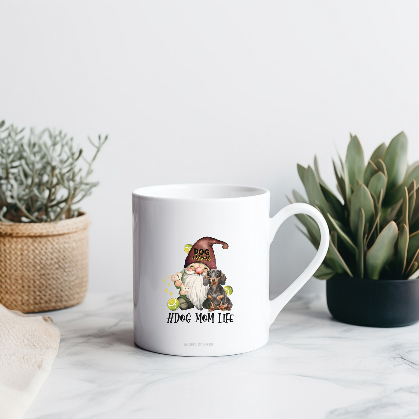 a mug with a gnome on it sitting next to a potted plant