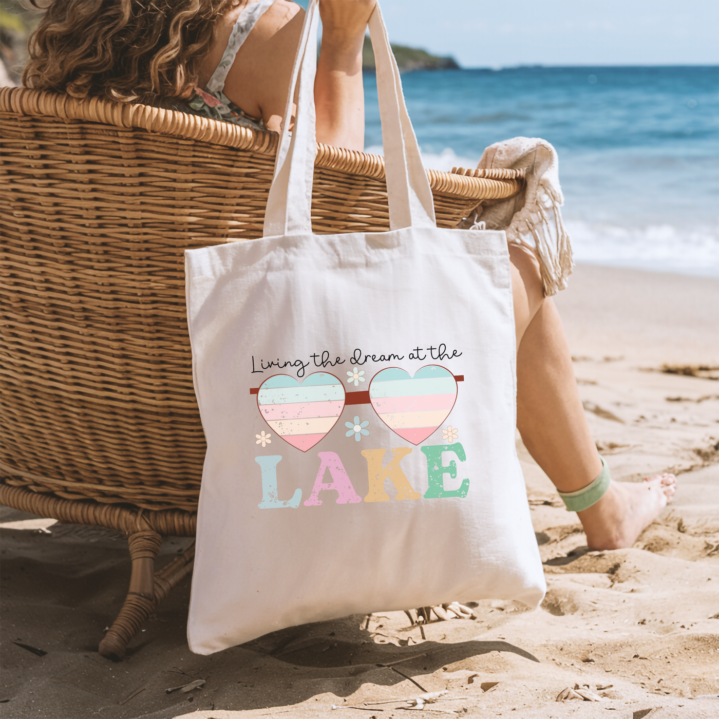 a woman sitting in a chair on the beach with a tote bag